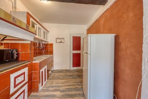 Eine schmale Küche mit Kühlschrank, Schränken und einer gefliesten Spritzschutzwand.
