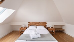 A bedroom with a sloped ceiling, a wooden headboard, two bedside tables, a bed with white linens, and a skylight. - La Houle - Bel appartement avec vue mer (Cancale)