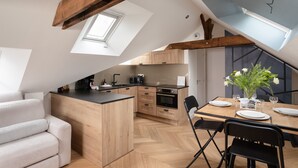 A modern kitchen with wooden cabinetry, a dining table set for two, and a lofted sleeping area. - La Houle - Bel appartement avec vue mer (Cancale)