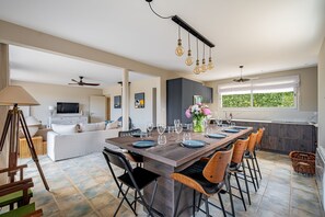 A modern kitchen with a dining area, a TV, and a ceiling fan. - Les Volets Bleus de Rhuys - Avec piscine privée (Saint-Gildas-de-Rhuys)