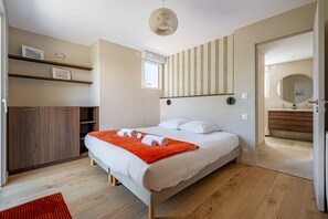 A bedroom with a bed, a wooden wardrobe, a red rug, a ceiling light, and a bathroom visible through an open door. - Les Volets Bleus de Rhuys - Avec piscine privée (Saint-Gildas-de-Rhuys)