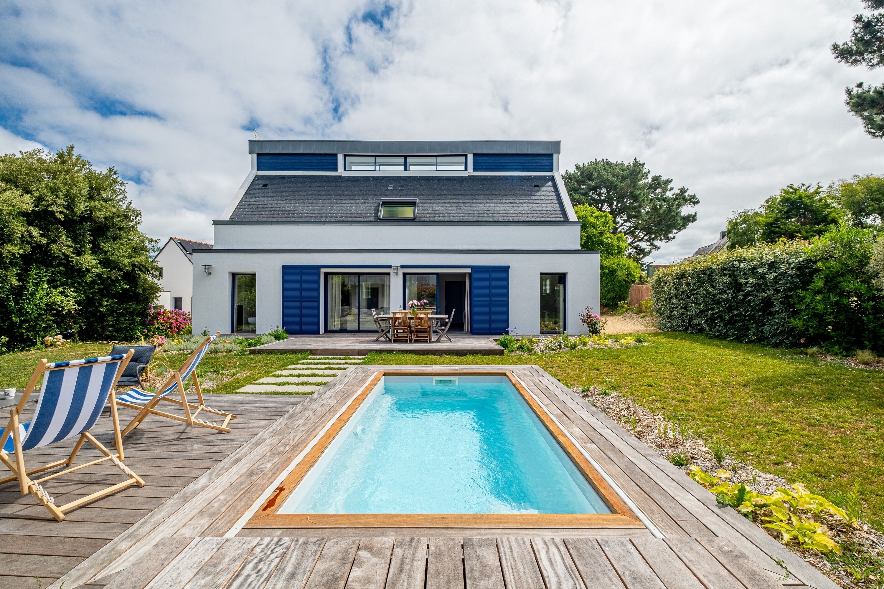 Une maison moderne dotée d’une piscine, de chaises longues et d’une table de patio.