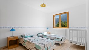A bedroom with two beds, a window with a mountain view, a radiator, and a nightstand with a lamp. - Le Nid de Ciambonson - Terrasse avec vue montagne (La Tour)