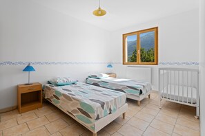 Ein Schlafzimmer mit zwei Betten, einem Fenster mit Blick auf die Berge, einem Heizkörper und einem Nachttisch mit Lampe.