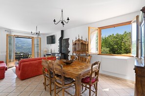 Ein Essbereich mit einem Holztisch und Stühlen, einem roten Sofa und Blick auf Grün hinter großen Fenstern.