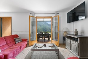 Ein Wohnzimmer mit einem roten Sofa, einem Couchtisch, einem Fernseher und Bergblick durch eine Glastür.