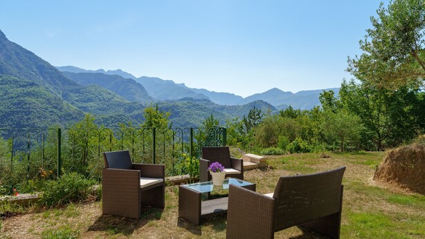 An outdoor seating area with wicker furniture and a glass table, overlooking a mountainous landscape. - Le Nid de Ciambonson - Terrasse avec vue montagne (La Tour)