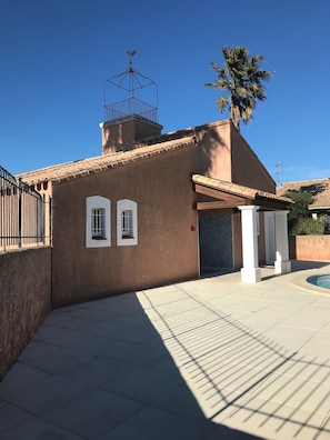 A building with a weather vane, a palm tree, and a tiled patio area.