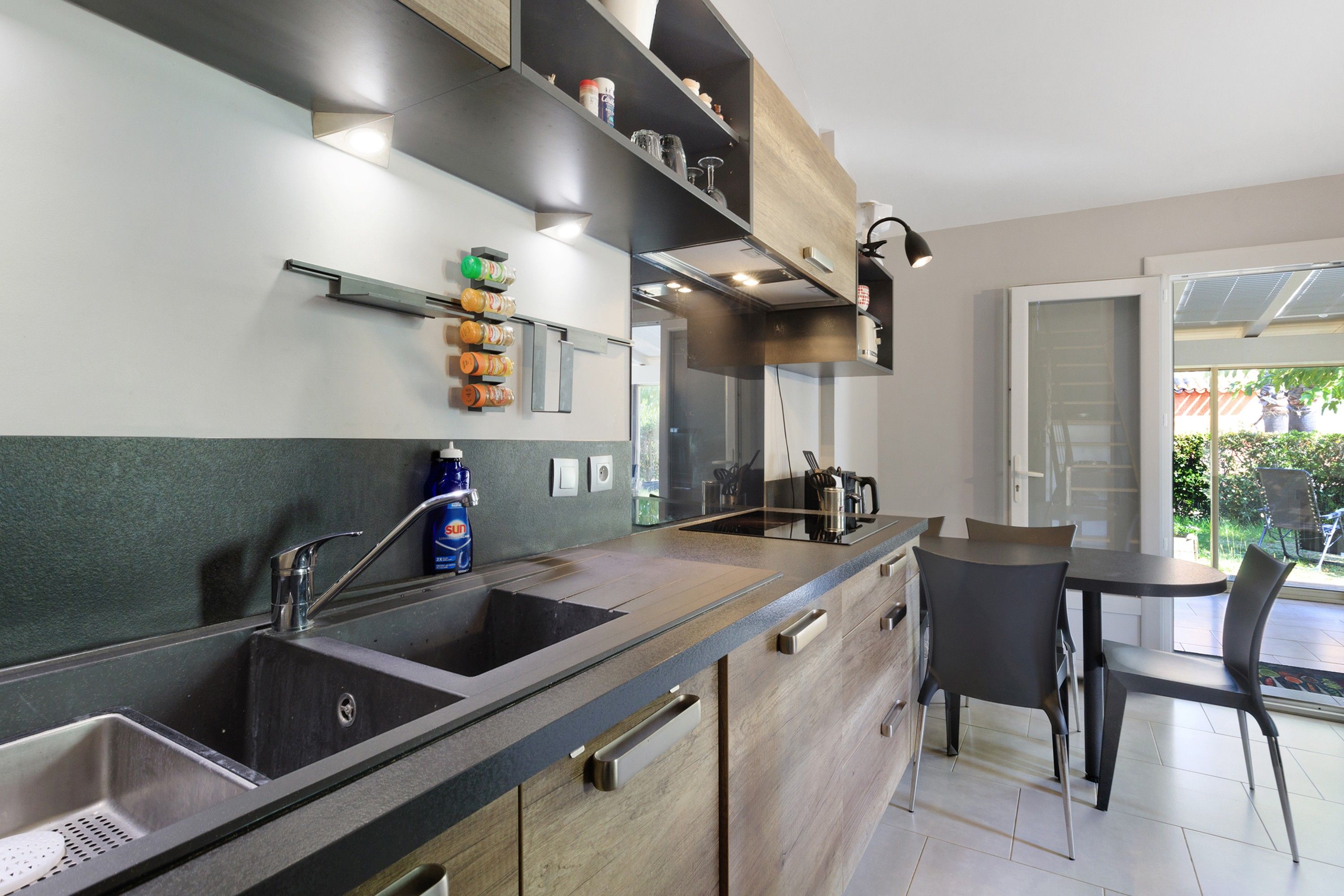 Een moderne keuken met een ingebouwde gootsteen, een eethoek met een tafel en stoelen, en uitzicht op de omgeving door een glazen deur.