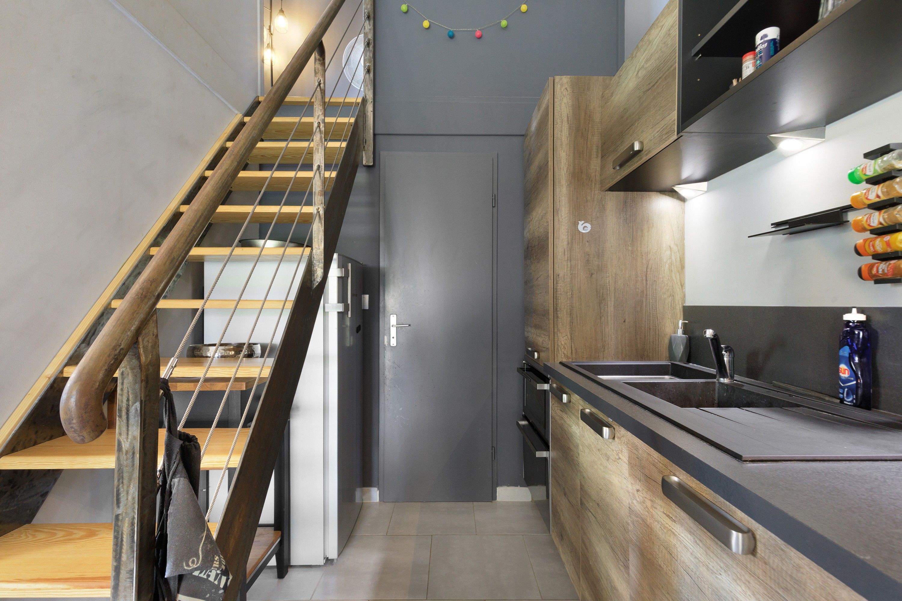 Cozinha moderna com escada de madeira, eletrodomésticos embutidos e bancada preta.