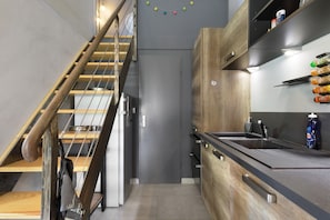 Une cuisine moderne avec un escalier en bois, des appareils électroménagers intégrés et un plan de travail noir.
