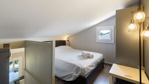 A bedroom with a bed, a bedside table, a lamp, and a window with a view.