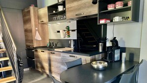 A modern kitchen with a central island, built-in shelves, and a staircase leading to another level.