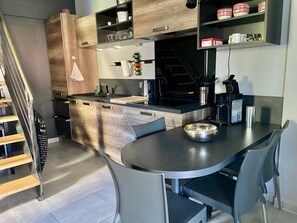 A modern kitchen with a central island, built-in shelves, and a staircase leading to another level.
