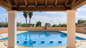 A swimming pool with a tiled deck, surrounded by palm trees and a clear sky.