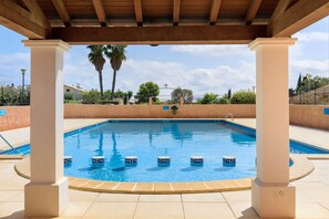 Una piscina con borde de baldosas, rodeada de palmeras y un cielo despejado.
