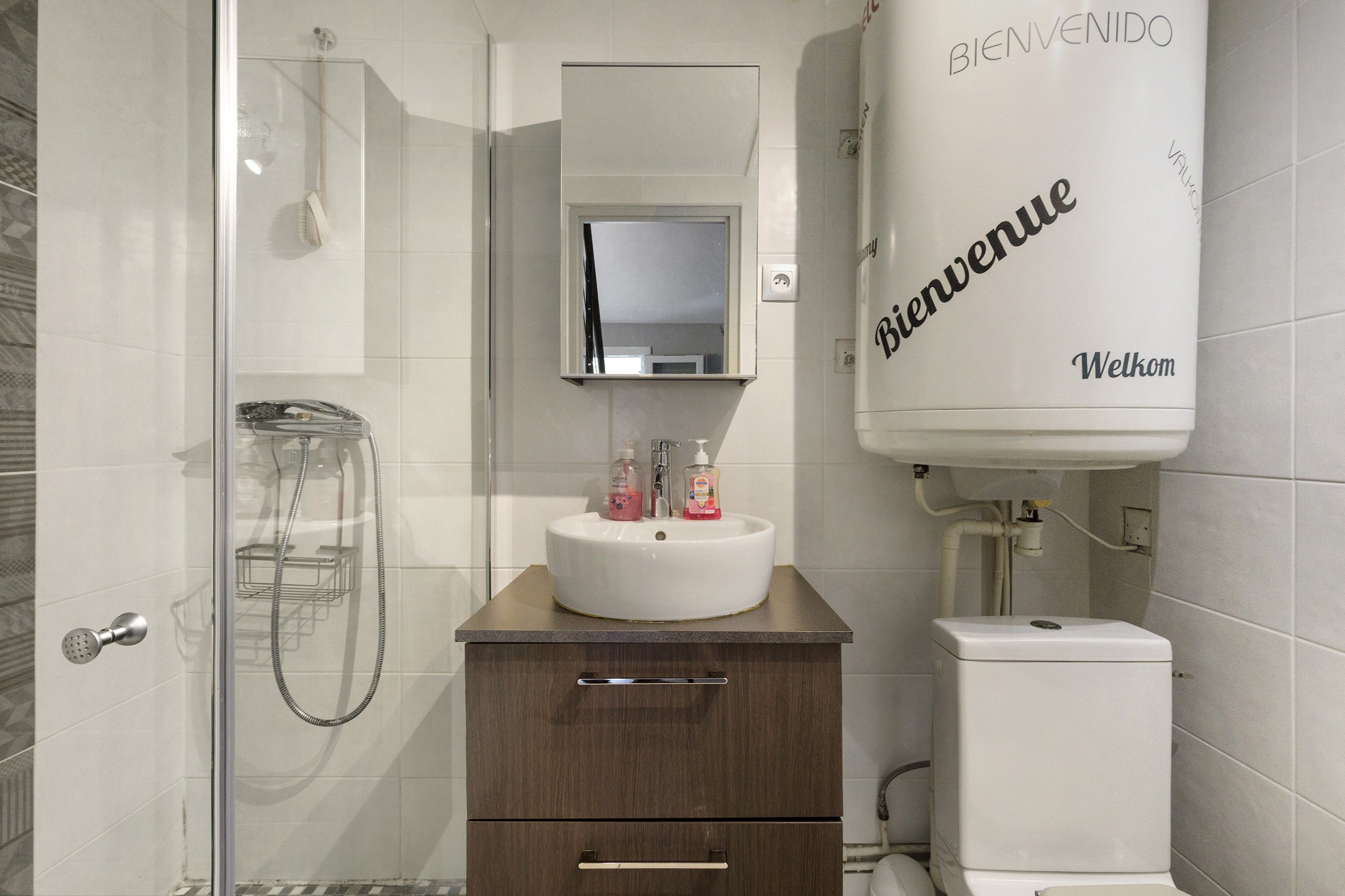 A bathroom with a shower, a sink with toiletries, a mirror, and a toilet.