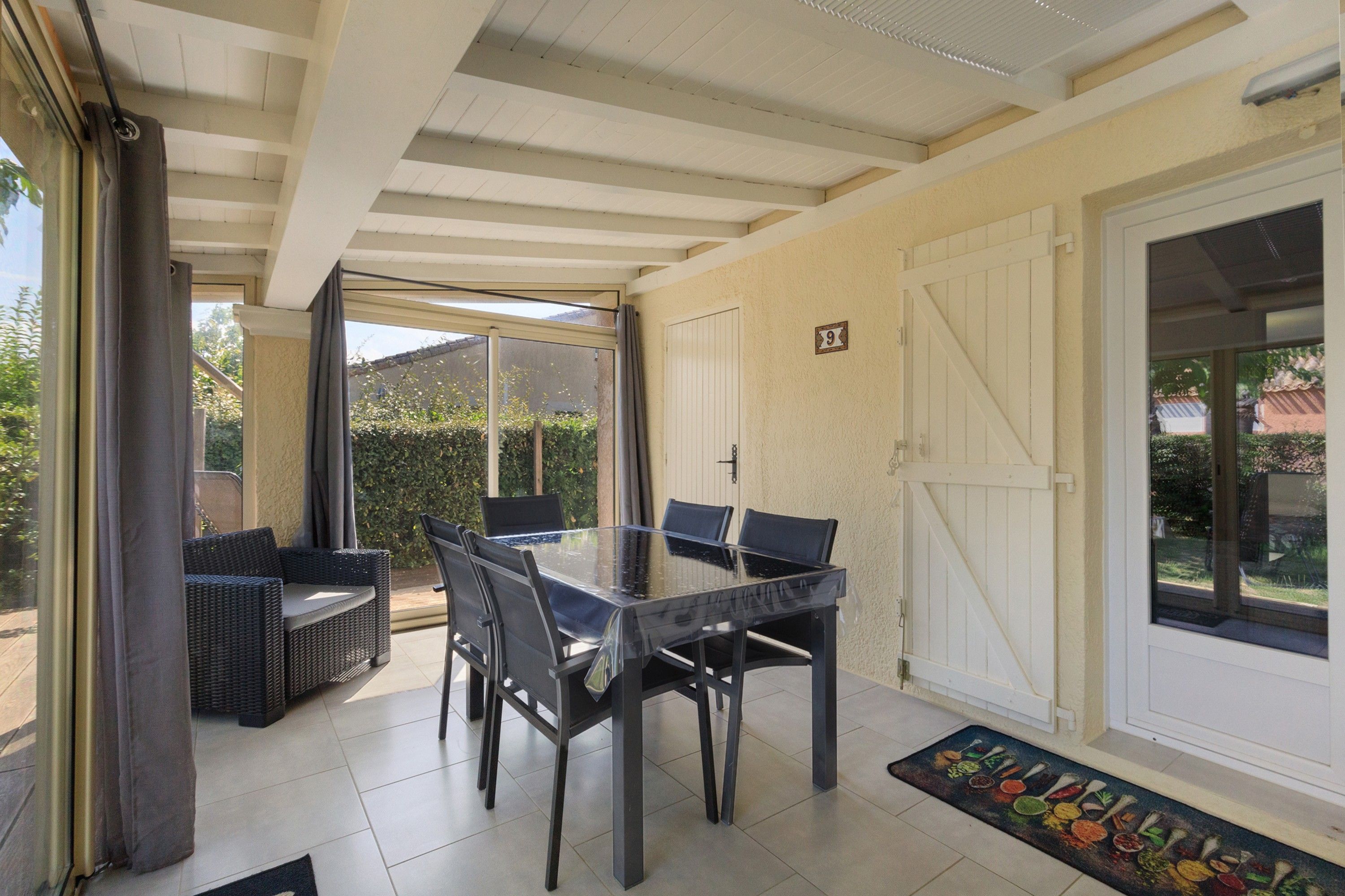 A covered patio area with a dining table and chairs, a wicker sofa, and a sliding glass door leading to a garden.