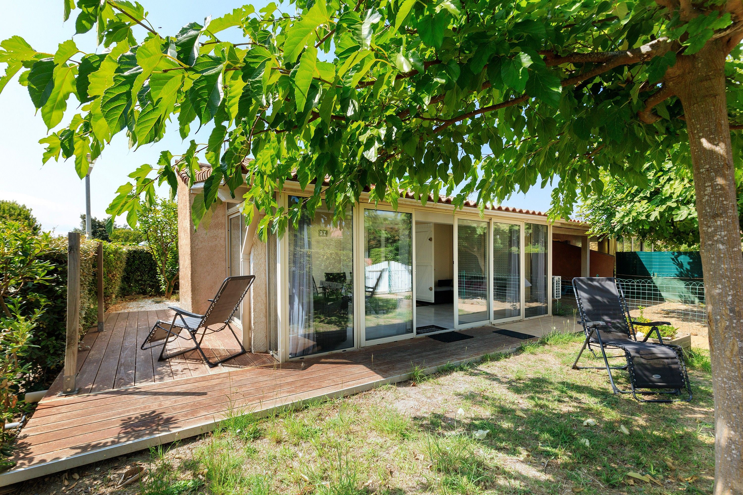 A covered outdoor seating area with two chairs, a wooden deck, and a glass-enclosed structure.