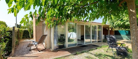 A covered outdoor seating area with two chairs, a wooden deck, and a glass-enclosed structure.