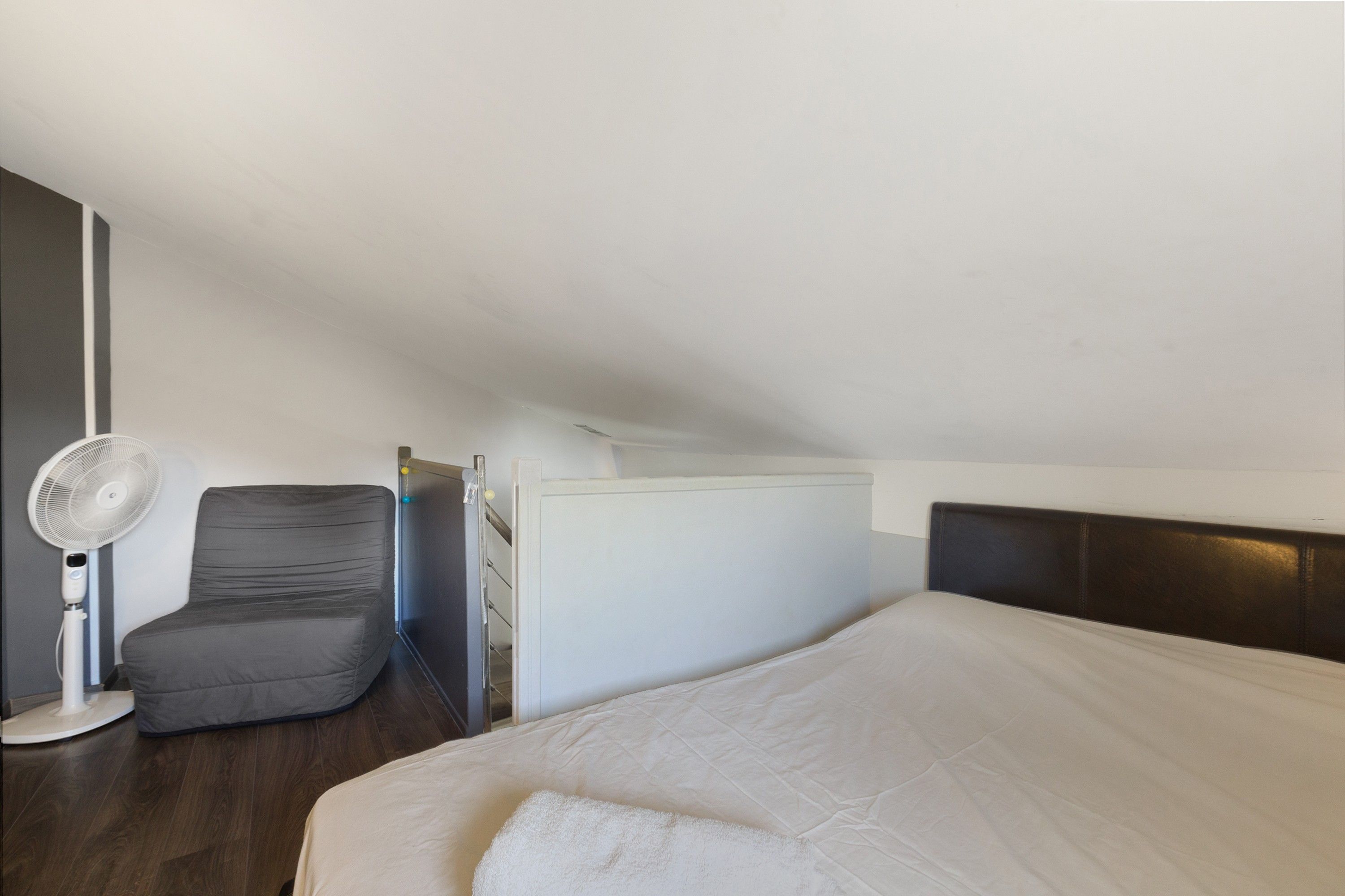 Un dormitorio con cama, una silla, un ventilador y una puerta.