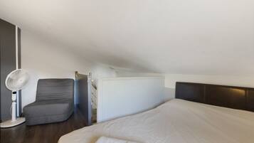 Un dormitorio con cama, una silla, un ventilador y una puerta.