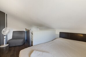 Un dormitorio con cama, una silla, un ventilador y una puerta.