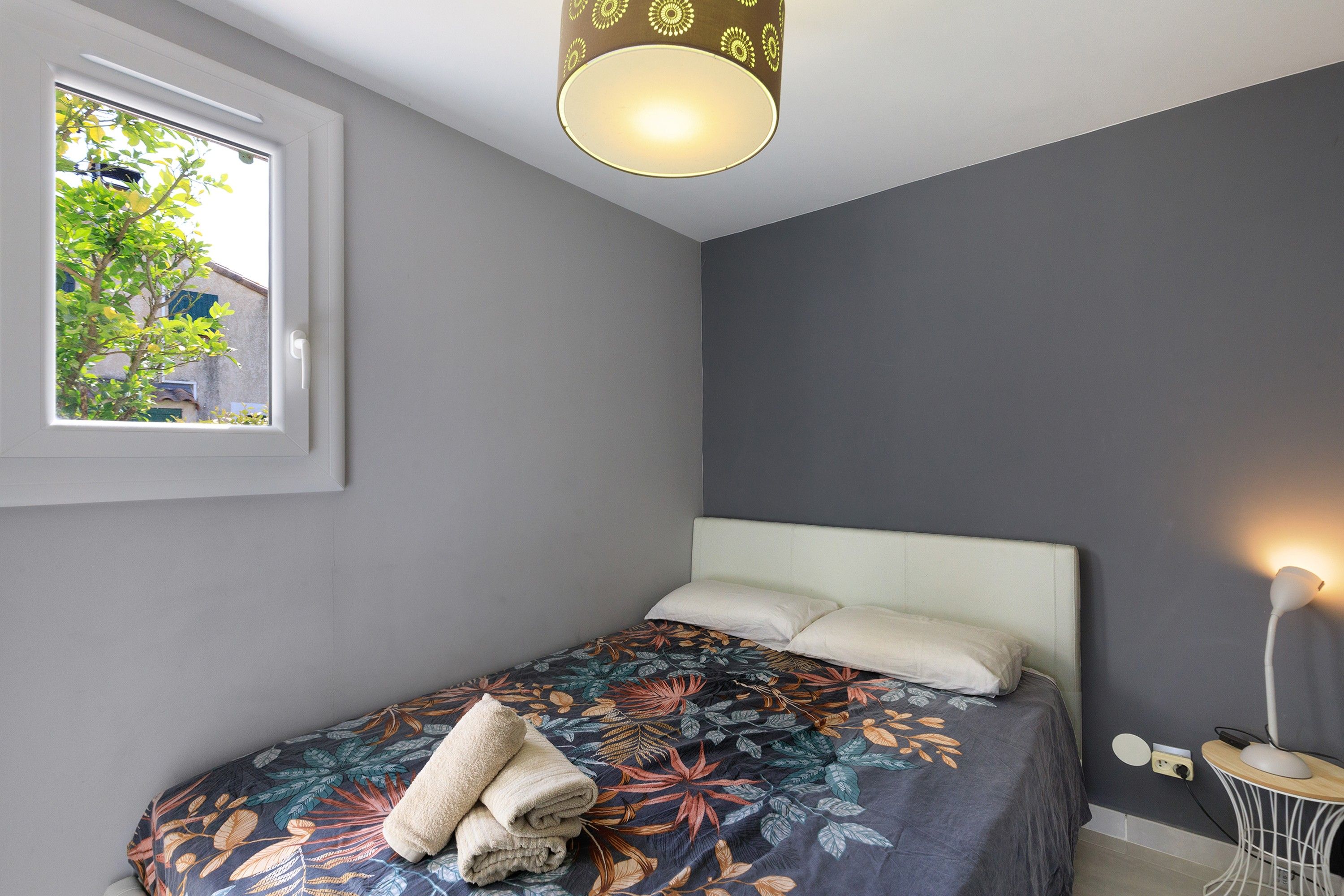Une chambre à coucher avec un lit, une fenêtre, une lampe de chevet et une vue sur la verdure.