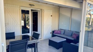 A covered outdoor area with a glass table and chairs, a sofa with cushions, and a sliding glass door leading to a patio.