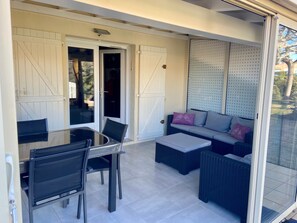 A covered outdoor area with a glass table and chairs, a sofa with cushions, and a sliding glass door leading to a patio.