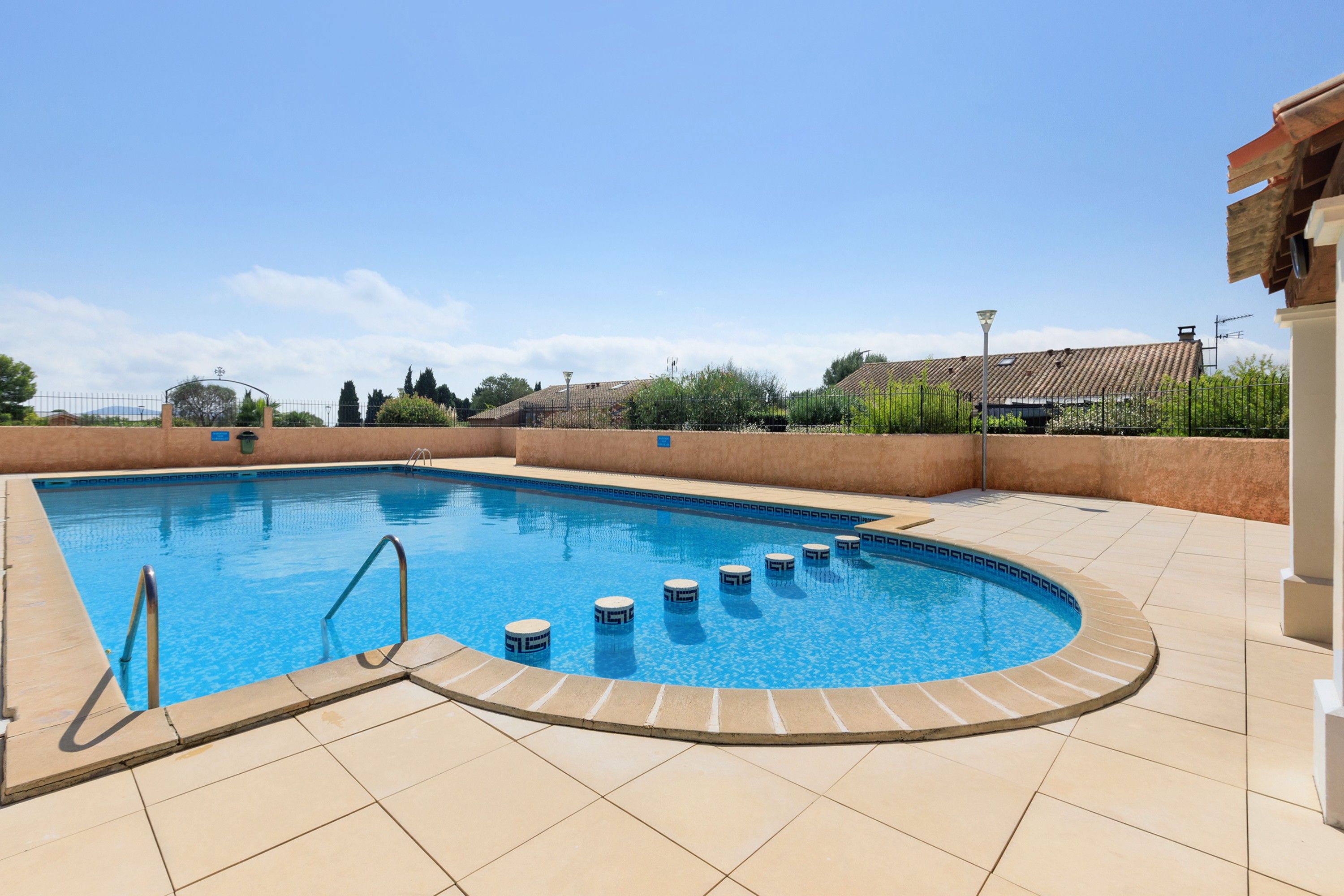 Una piscina con borde curvo, una escalera de metal y un deck con azulejos.