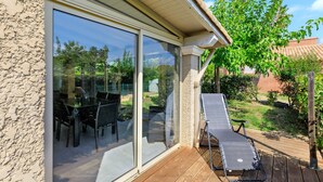 A patio with a table and chairs, a sun lounger, and a glass door leading to an outdoor area.
