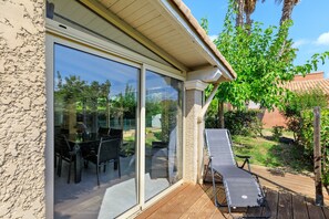 Un patio con una mesa, sillas, una tumbona y un ventanal de vidrio que da a un espacio al aire libre.