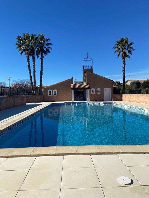 A swimming pool with a tiled deck, a building with a tiled roof, and palm trees.