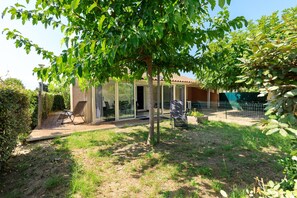 Una casa con puerta de vidrio, un patio con una silla y un jardín cercado.