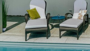 Two wicker lounge chairs with white cushions and a small round table with a glass top.