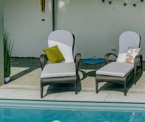 Two wicker lounge chairs with white cushions and a small round table with a glass top.