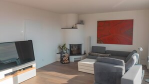 A modern living room with a flat-screen TV, a fireplace, a grey sofa, and a red abstract painting.