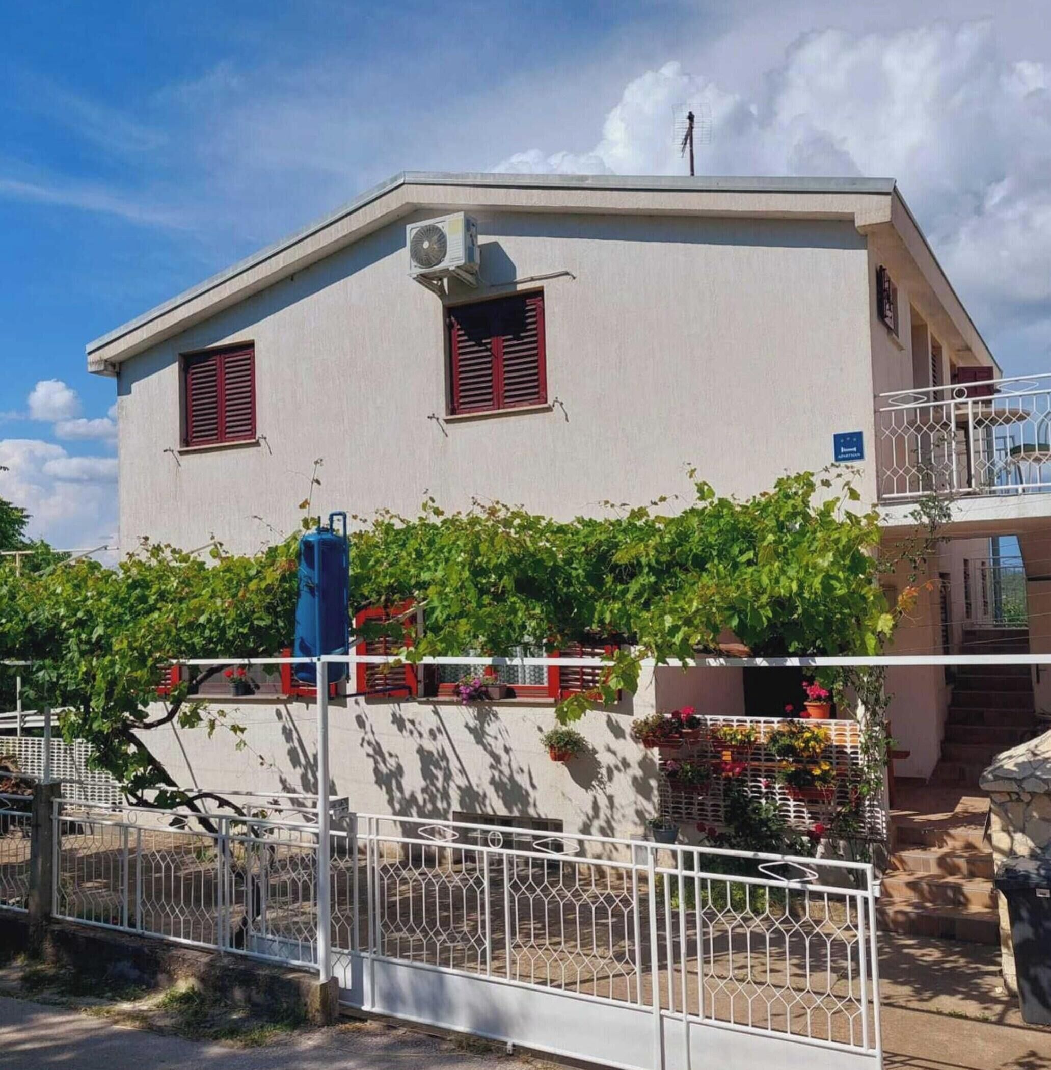 A two-story building with a flat roof, a balcony on the upper floor, and a small air conditioning unit on the wall.