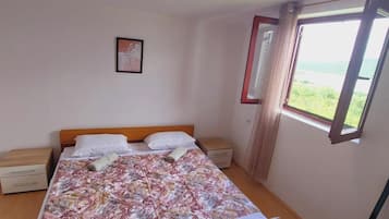 A single bed with a floral bedspread, a nightstand, a small drawer, and a window with a view of greenery.