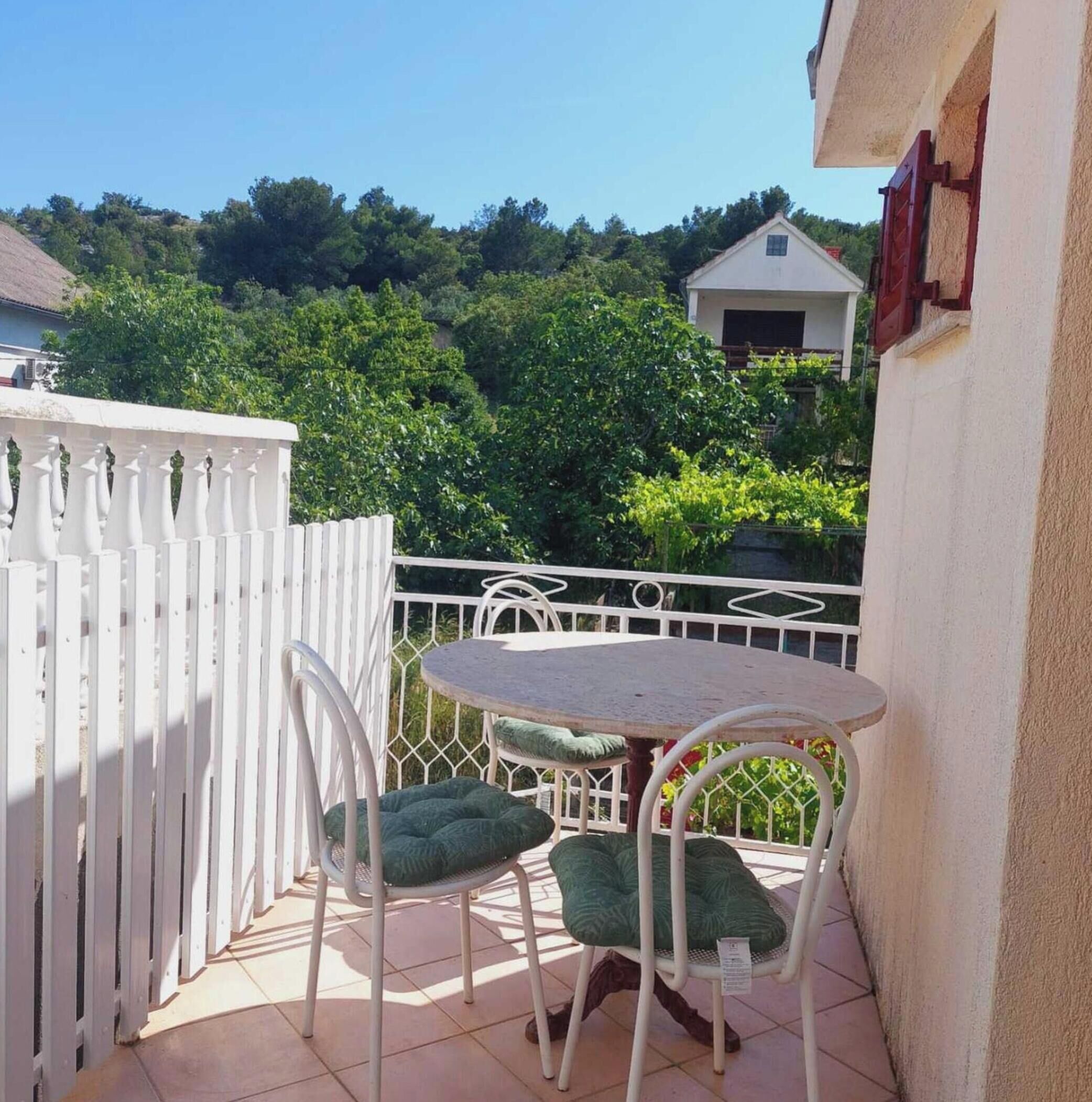 A small outdoor patio with a round table and two chairs, a white fence, and a house in the background.
