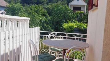 A small outdoor patio with a round table and two chairs, a white fence, and a house in the background.