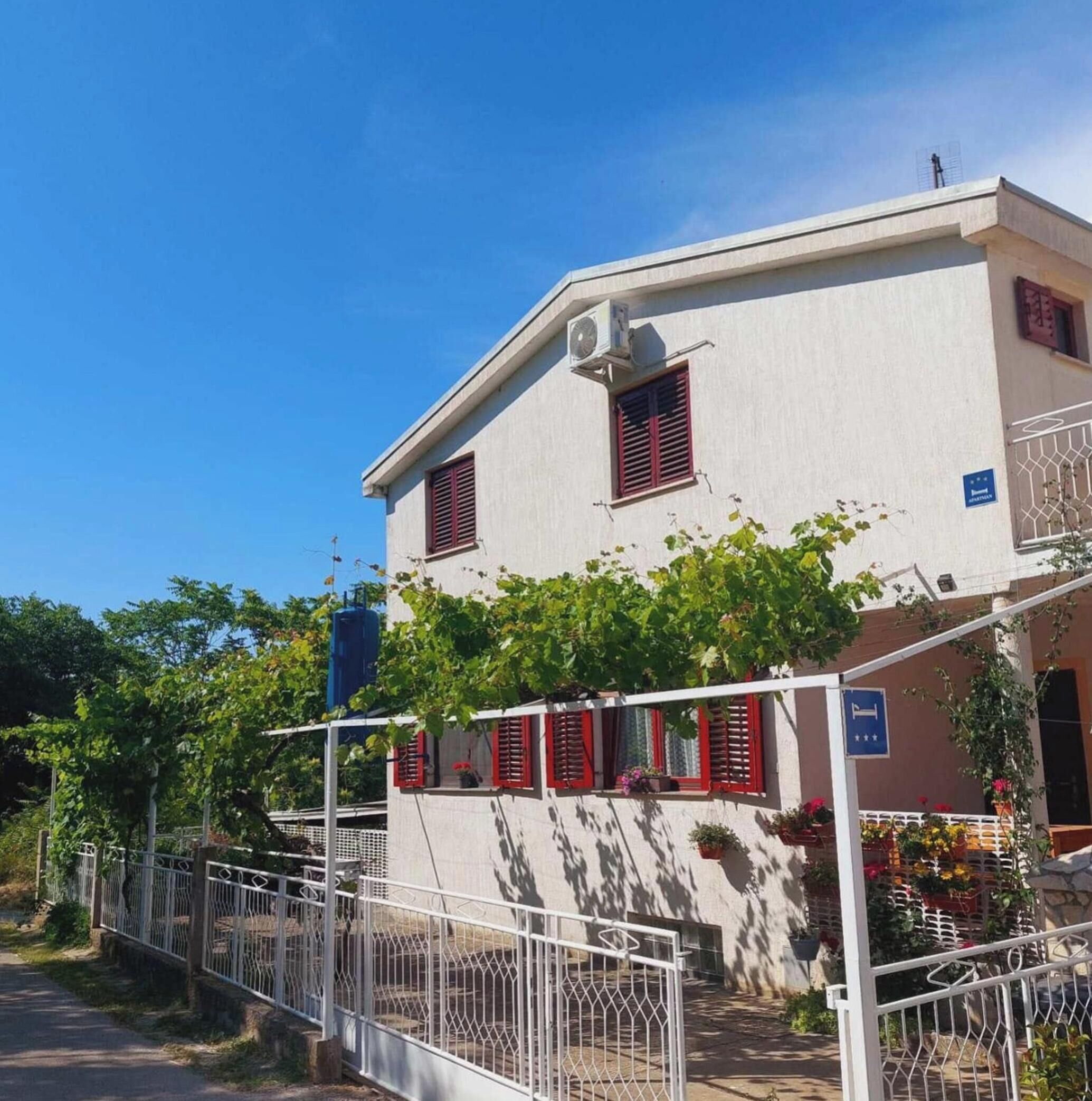 A two-story building with a white facade, red shutters, and a metal gate.