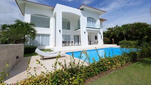 Ein zweistöckiges Haus mit Swimmingpool, umgeben von Grünpflanzen und Palmen.