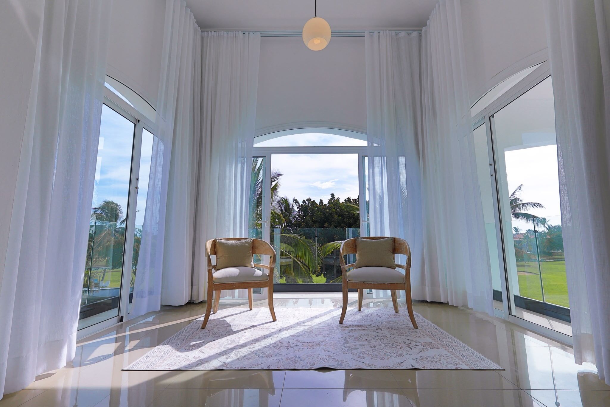 A room with two chairs, a white rug, and large windows with curtains.