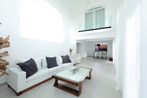 A modern living room with a glass coffee table, white sofa, and a dining area in the background. - Spacious 4-bedroom house in serene Punta Cana with AC (Punta Cana)