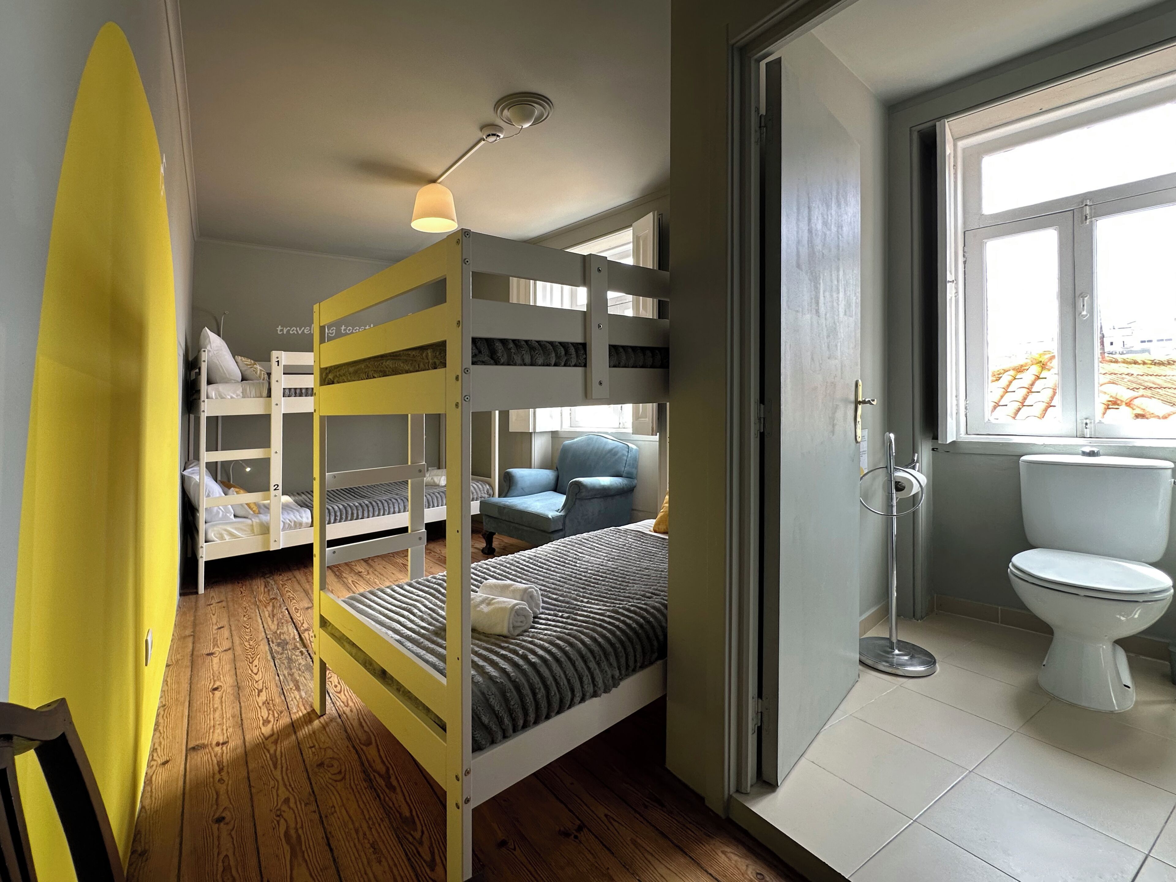 A room with bunk beds, a chair, a surfboard, and a toilet.