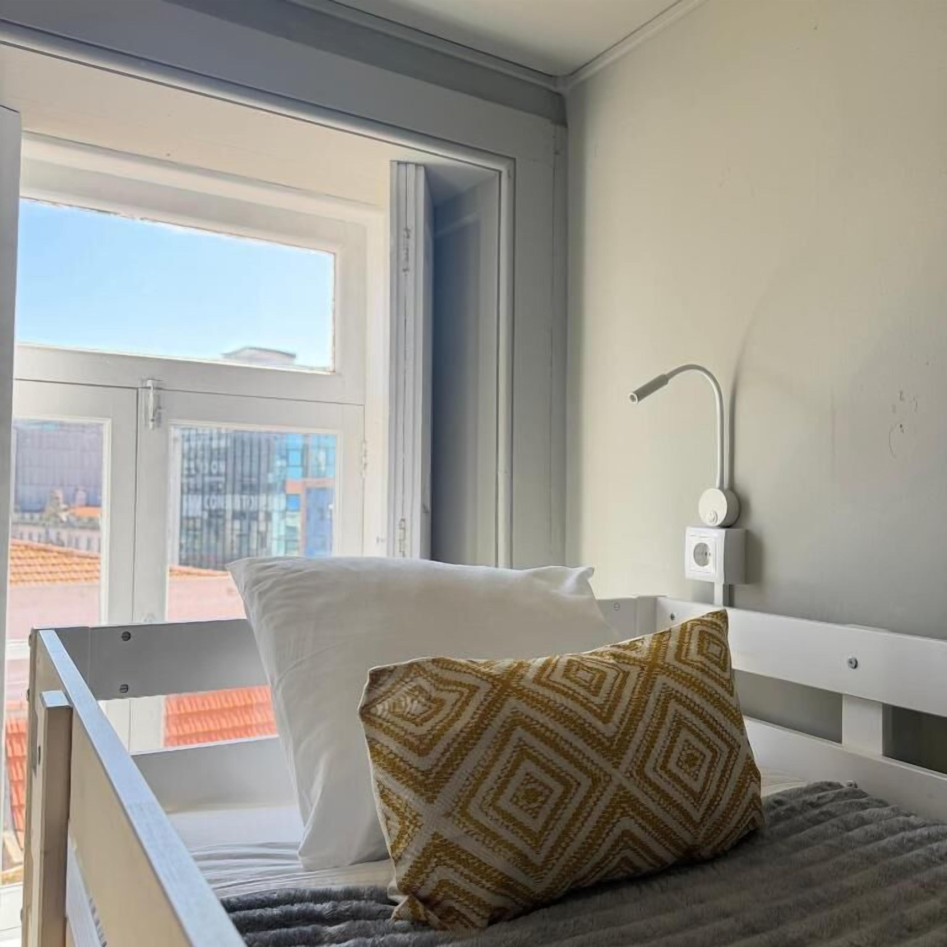 Una habitación con cama, ventana y vistas a edificios.