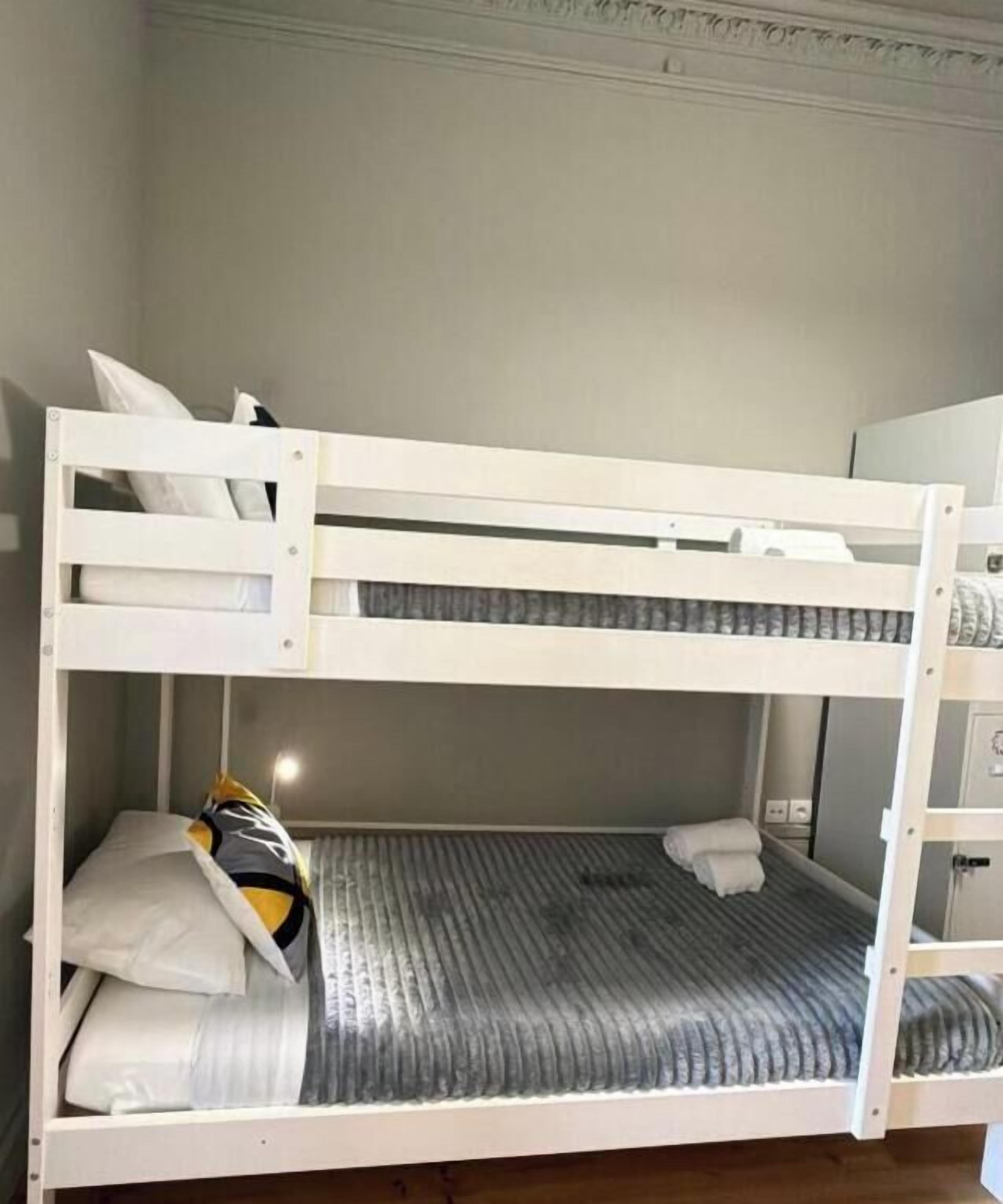 A bunk bed with a mattress and pillows, a wooden floor, and a white wall.