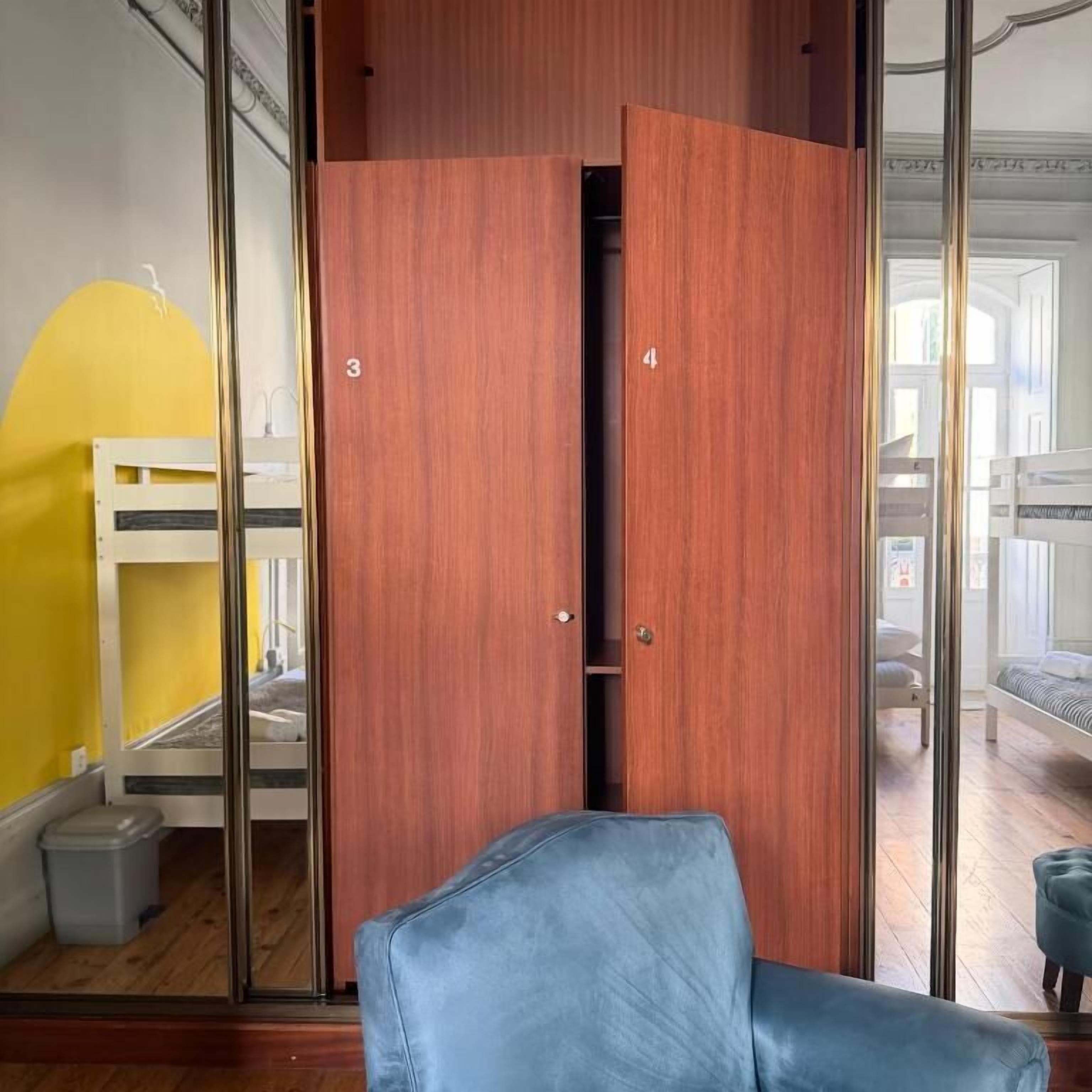 A room with a wooden wardrobe, a blue chair, and a bunk bed in the background.